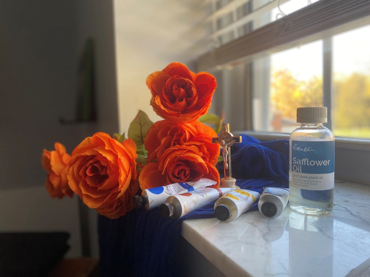 Orange flowers on a table with a crucifix, oil paints, and a bottle of safflower oil in the background.